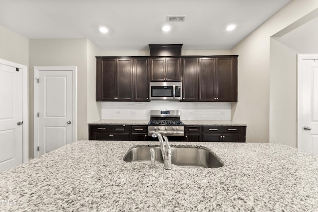 409 Rhamkatte Rd, Holly Springs, NC 27540 - kitchen with stainless steel appliances, a sink, dark brown cabinetry, tasteful backsplash, and light stone counters