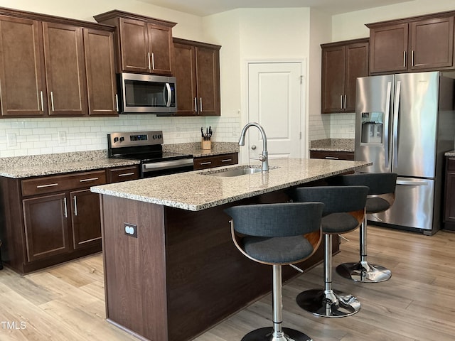 1116 Sidney Creek Dr Unit 1116, Zebulon, NC 27597 - kitchen with appliances with stainless steel finishes, a sink, light wood-type flooring, a kitchen breakfast bar, and light stone countertops