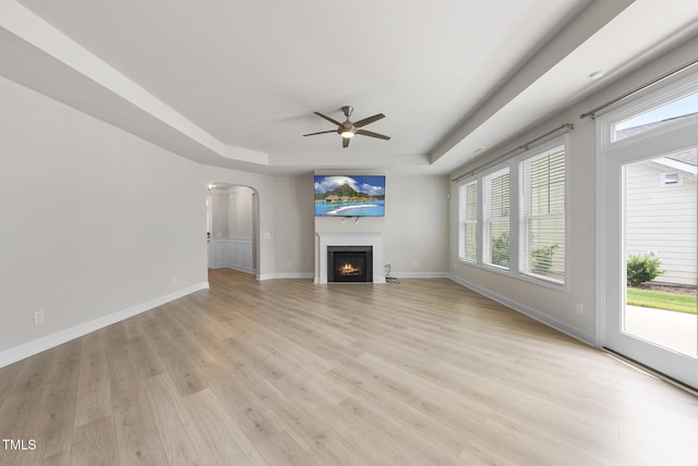 537 Bramble Ln, Clayton, NC 27527 - unfurnished living room featuring a raised ceiling, a ceiling fan, light wood-style flooring, arched walkways, and a lit fireplace