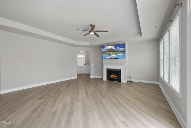 537 Bramble Ln, Clayton, NC 27527 - unfurnished living room with a tray ceiling, a ceiling fan, light wood-type flooring, a warm lit fireplace, and arched walkways