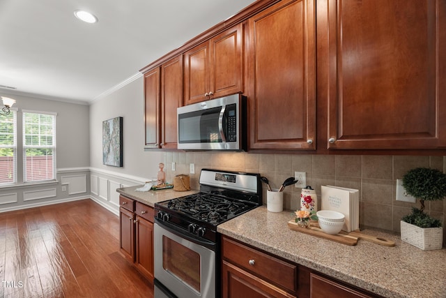 7873 Cape Charles Dr, Raleigh, NC 27617 - kitchen with appliances with stainless steel finishes, ornamental molding, dark wood-type flooring, light stone countertops, and wainscoting