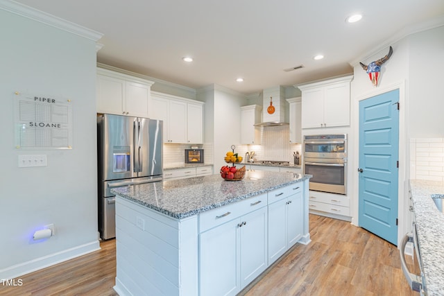 470 E Wellesley Dr, Clayton, NC 27520 - kitchen featuring appliances with stainless steel finishes, ornamental molding, a kitchen island, light wood-style floors, and wall chimney range hood