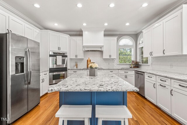 206 W Stoneybrook Ct, Benson, NC 27504 - kitchen featuring stainless steel appliances, ornamental molding, a center island, white cabinets, and light wood-style flooring