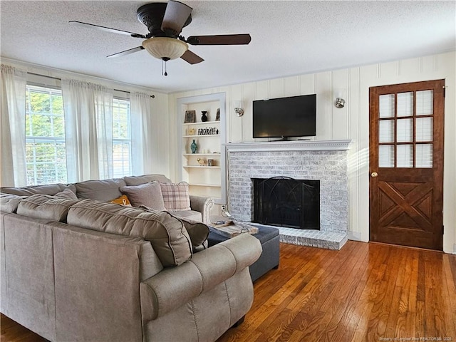 3647 Olivia Rd, Sanford, NC 27332 - living room with a textured ceiling, a brick fireplace, wood finished floors, built in features, and a ceiling fan