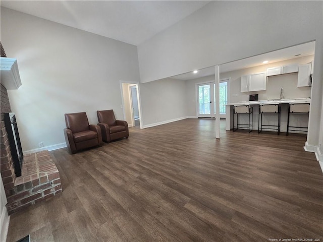 409 Thimbleberry Dr, Vass, NC 28394 - unfurnished living room featuring a brick fireplace, dark wood-type flooring, baseboards, and a towering ceiling