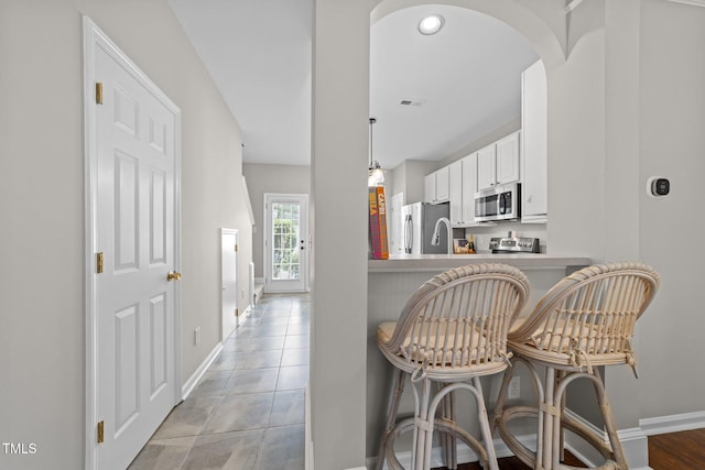 5717 Corbon Crest Ln, Raleigh, NC 27612 - kitchen with appliances with stainless steel finishes, arched walkways, a kitchen breakfast bar, white cabinetry, and decorative light fixtures