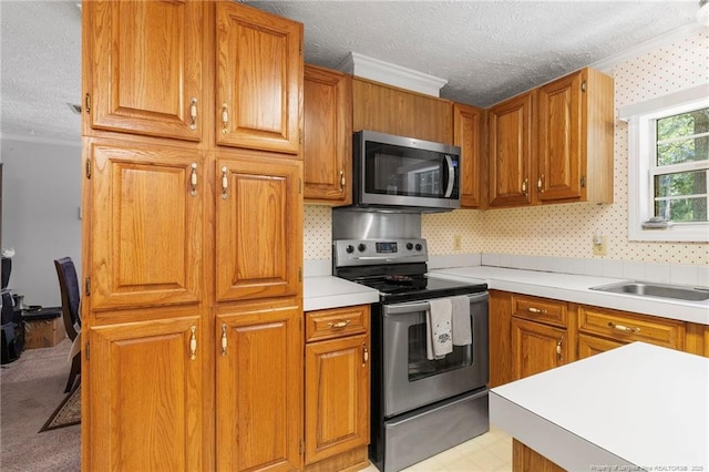 21621 Old Maxton Rd, Maxton, NC 28364 - kitchen featuring stainless steel appliances, a textured ceiling, ornamental molding, light countertops, and brown cabinets