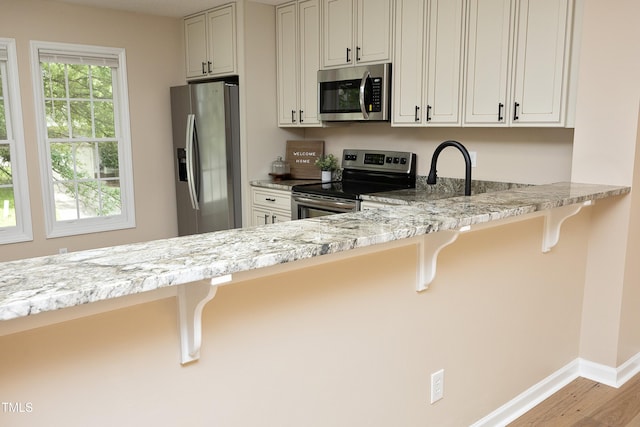 105 Old Dock Trl, Cary, NC 27519 - kitchen with stainless steel appliances, wood finished floors, baseboards, a breakfast bar, and light stone counters