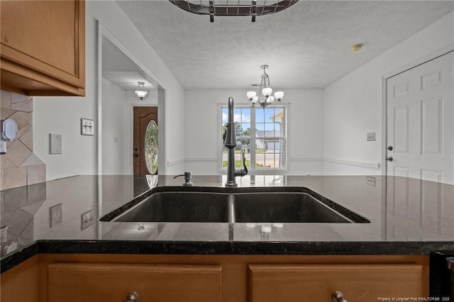 107 Hayes Ct, Raeford, NC 28376 - kitchen with a sink, brown cabinetry, dark stone countertops, a chandelier, and a textured ceiling
