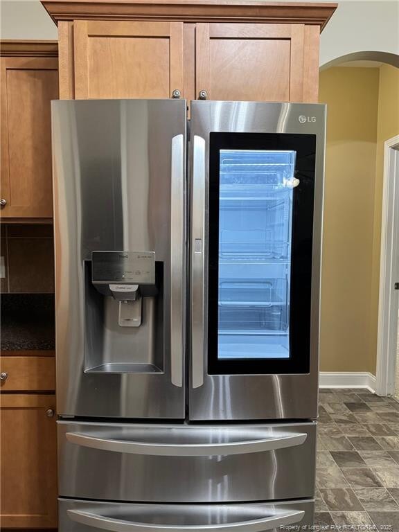 1545 Gallant Fox Ct, Parkton, NC 28371 - kitchen view of stainless steel refrigerator with ice dispenser, brown cabinets, arched walkways, dark countertops, and baseboards