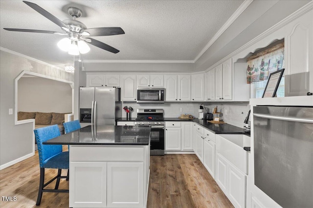 9801 Honeycutt Rd, Raleigh, NC 27614 - kitchen featuring stainless steel appliances, ornamental molding, white cabinetry, a kitchen breakfast bar, and wood finished floors