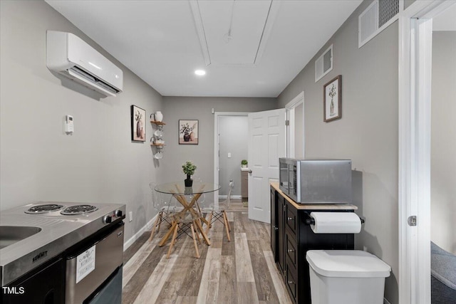 9801 Honeycutt Rd, Raleigh, NC 27614 - kitchen featuring stainless steel microwave, light wood-style flooring, a wall unit AC, dark cabinetry, and baseboards