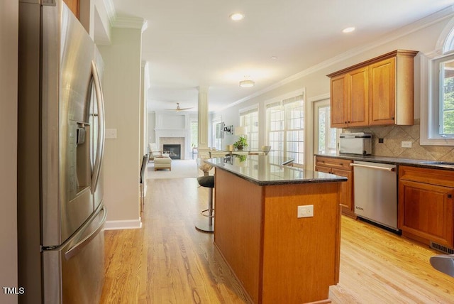 1005 Hidden River Ct, Raleigh, NC 27614 - kitchen with appliances with stainless steel finishes, a kitchen island, brown cabinets, light wood-style flooring, and ornamental molding