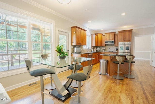 1005 Hidden River Ct, Raleigh, NC 27614 - kitchen featuring appliances with stainless steel finishes, brown cabinets, dark countertops, backsplash, and crown molding