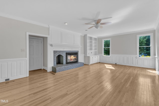 6201 Bayswater Trl, Raleigh, NC 27612 - unfurnished living room featuring ceiling fan, ornamental molding, light wood-type flooring, wainscoting, and a brick fireplace