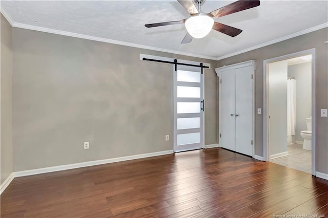 1519 Magnolia Dr, Fairmont, NC 28340 - unfurnished bedroom featuring a barn door, wood finished floors, baseboards, ensuite bath, and ornamental molding