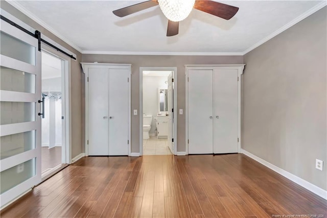 1519 Magnolia Dr, Fairmont, NC 28340 - unfurnished bedroom with a barn door, wood finished floors, baseboards, ensuite bathroom, and ceiling fan