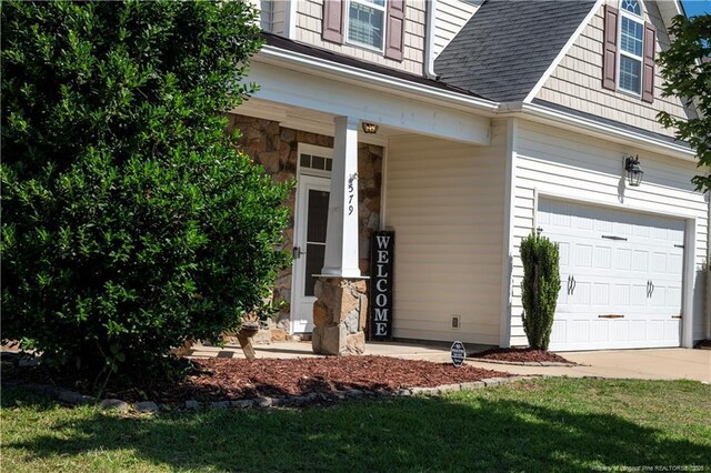 579 Wedgefield Dr, Raeford, NC 28376 - view of exterior entry featuring a garage, roof with shingles, concrete driveway, a porch, and stone siding