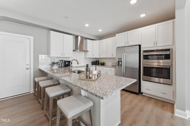 144 N White St # 100, Wake Forest, NC 27587 - kitchen featuring appliances with stainless steel finishes, wall chimney exhaust hood, a peninsula, white cabinetry, and a kitchen breakfast bar