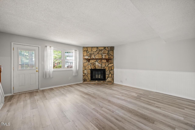 7731 Kingsberry Ct, Raleigh, NC 27615 - unfurnished living room featuring a textured ceiling, light wood-style floors, a stone fireplace, and a wainscoted wall