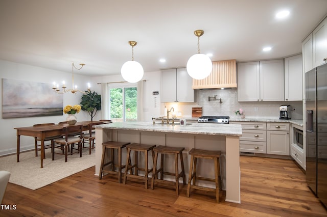 5012 Skidmore St, Raleigh, NC 27609 - kitchen with wood finished floors, light stone counters, tasteful backsplash, appliances with stainless steel finishes, and a center island with sink