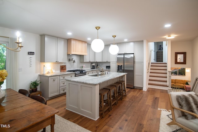 5012 Skidmore St, Raleigh, NC 27609 - kitchen featuring appliances with stainless steel finishes, light stone counters, dark wood finished floors, an island with sink, and a breakfast bar