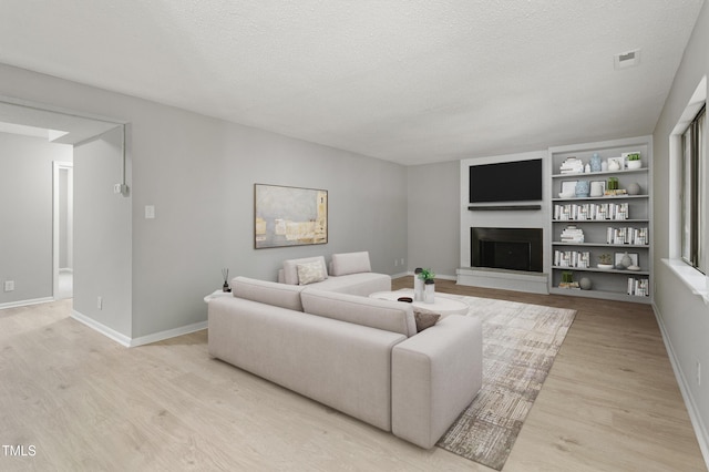 3088 Colony Rd Unit A, Durham, NC 27705 - living area with light wood-style flooring, a fireplace with raised hearth, built in shelves, a textured ceiling, and baseboards