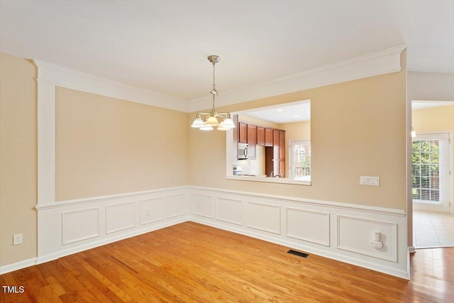2614 Laurelcherry St, Raleigh, NC 27612 - unfurnished dining area with light wood-type flooring, a chandelier, crown molding, and wainscoting