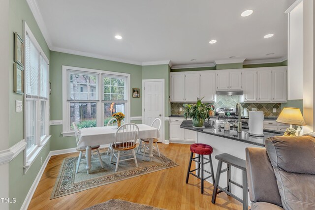 7613 Percy Ct, Raleigh, NC 27613 - kitchen with under cabinet range hood, white cabinetry, light wood finished floors, tasteful backsplash, and a breakfast bar area
