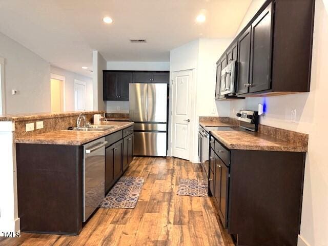 820 Houston Ct, Haw River, NC 27258 - kitchen featuring appliances with stainless steel finishes, a sink, light wood-style flooring, dark brown cabinetry, and an island with sink