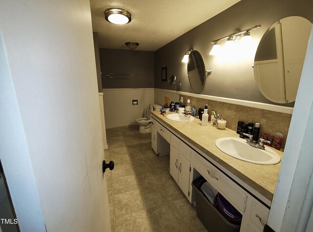 339 E Meadow Rd, Eden, NC 27288 - bathroom with a textured ceiling, toilet, double vanity, and wainscoting