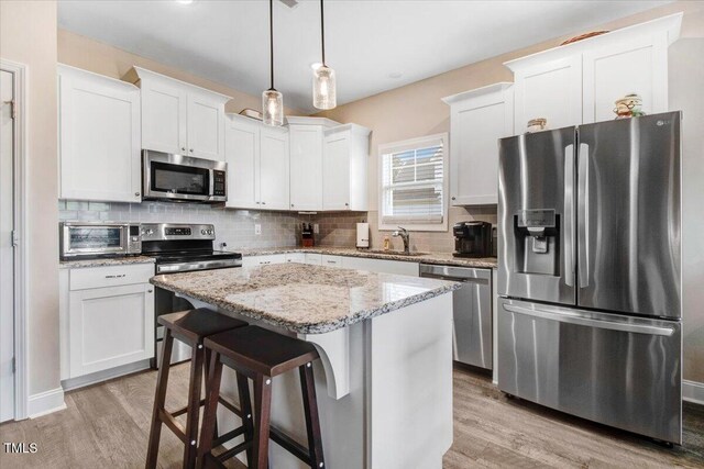 607 Laurel Lake Rd, Salemburg, NC 28385 - kitchen with stainless steel appliances, a sink, light wood finished floors, decorative backsplash, and white cabinetry