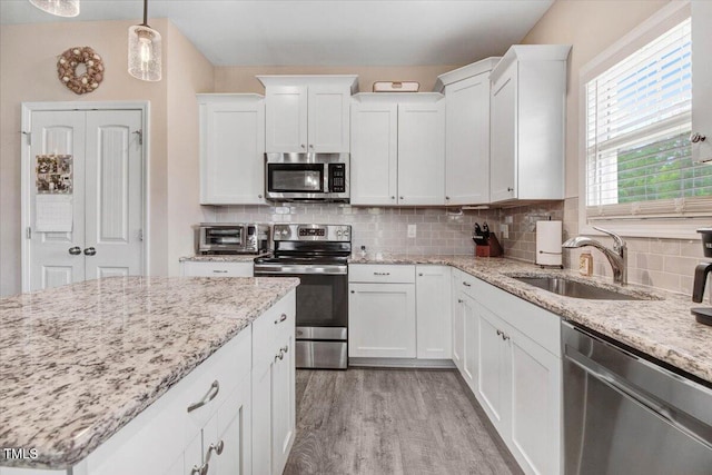 607 Laurel Lake Rd, Salemburg, NC 28385 - kitchen with stainless steel appliances, a sink, light wood finished floors, white cabinets, and decorative backsplash