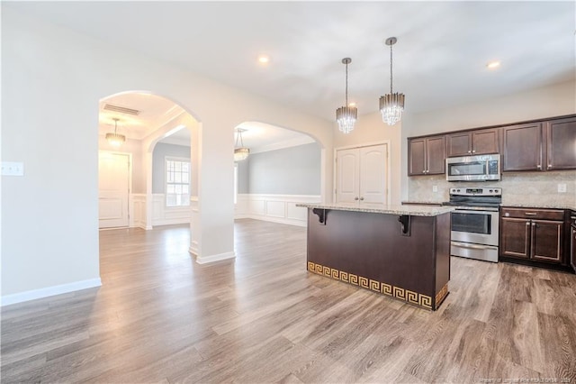 2912 Seafarer Dr, Fayetteville, NC 28306 - kitchen featuring appliances with stainless steel finishes, a kitchen bar, arched walkways, dark brown cabinets, and light stone counters