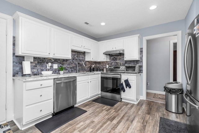 1516 Greys Mill Rd, Rocky Mount, NC 27804 - kitchen with appliances with stainless steel finishes, under cabinet range hood, white cabinets, decorative backsplash, and wood finished floors