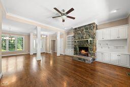 311 Rassie Crabtree Rd, Rougemont, NC 27572 - unfurnished living room featuring ornate columns, crown molding, wood finished floors, a stone fireplace, and ceiling fan