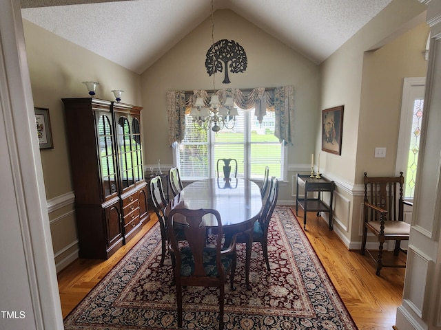 3409 Bennyfield Ct, Fuquay Varina, NC 27526 - dining area with a chandelier, lofted ceiling, light wood-style floors, a textured ceiling, and wainscoting
