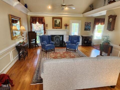 3409 Bennyfield Ct, Fuquay Varina, NC 27526 - living room featuring a fireplace, ceiling fan, a decorative wall, crown molding, and a wainscoted wall