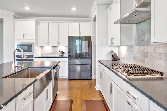 121 Canyon Gap Way, Raleigh, NC 27610 - kitchen featuring appliances with stainless steel finishes, wall chimney exhaust hood, white cabinetry, decorative backsplash, and ornamental molding