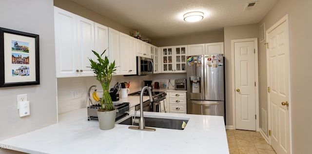 1911 Falls Landing Dr Unit 103, Raleigh, NC 27614 - kitchen with appliances with stainless steel finishes, glass insert cabinets, a peninsula, light countertops, and white cabinets