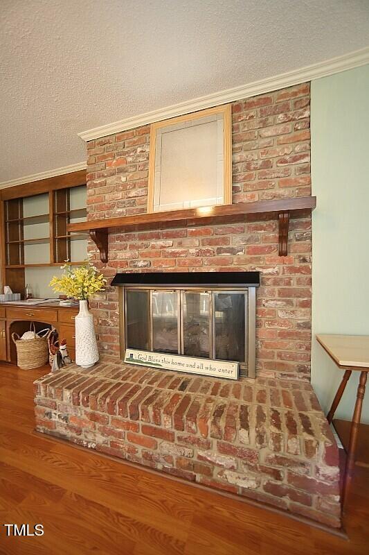 6717 Valley Dr, Raleigh, NC 27612 - detailed view of a brick fireplace, ornamental molding, a textured ceiling, and wood finished floors