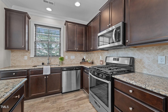 801 Socata Ln, Mebane, NC 27302 - kitchen with stainless steel appliances, dark brown cabinetry, ornamental molding, light stone countertops, and light wood-style flooring