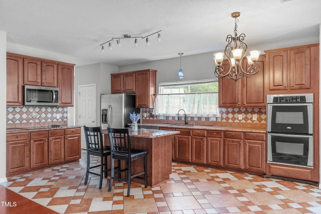 760 Stackhurst Way, Wake Forest, NC 27587 - kitchen with appliances with stainless steel finishes, a chandelier, a kitchen island, brown cabinetry, and a textured ceiling