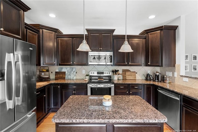 951 Whispering Pines Dr, Spring Lake, NC 28390 - kitchen featuring appliances with stainless steel finishes, dark brown cabinetry, a kitchen island, light stone counters, and decorative backsplash