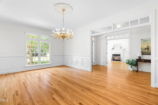 619 Baybush Dr, Raleigh, NC 27615 - unfurnished living room with a chandelier, ornamental molding, a glass covered fireplace, light wood finished floors, and a wainscoted wall