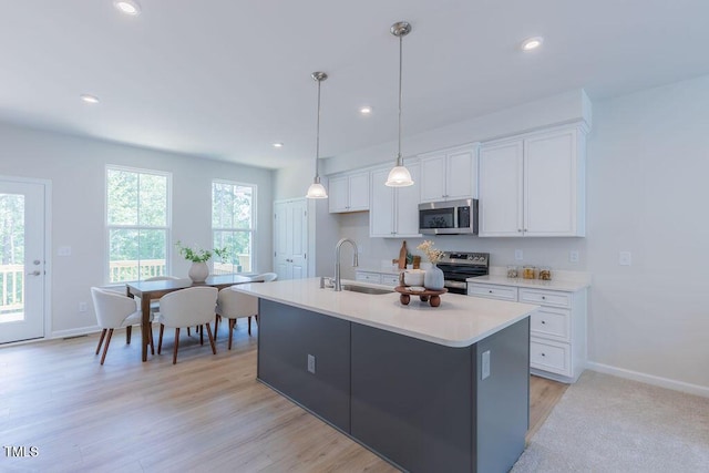 1359 Chowan Ave, Durham, NC 27713 - kitchen featuring appliances with stainless steel finishes, white cabinetry, light countertops, an island with sink, and hanging light fixtures