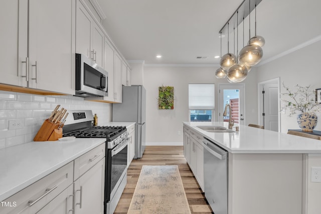 1729 Starlit Sky Ln, Cary, NC 27519 - kitchen featuring appliances with stainless steel finishes, an island with sink, backsplash, ornamental molding, and light countertops