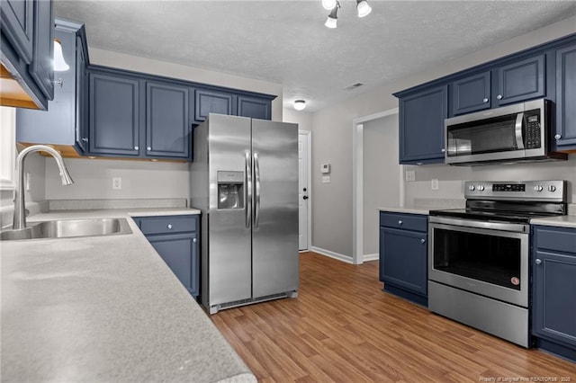 107 Beaumont Ct, Raeford, NC 28376 - kitchen featuring appliances with stainless steel finishes, a sink, blue cabinetry, light countertops, and light wood finished floors