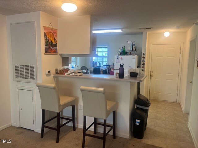 2000 University Woods Rd Unit 203, Raleigh, NC 27603 - kitchen with a breakfast bar, freestanding refrigerator, a textured ceiling, baseboards, and a peninsula