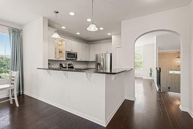 9141 Falkwood Rd, Raleigh, NC 27617 - kitchen featuring appliances with stainless steel finishes, arched walkways, glass insert cabinets, a kitchen bar, and dark wood-type flooring